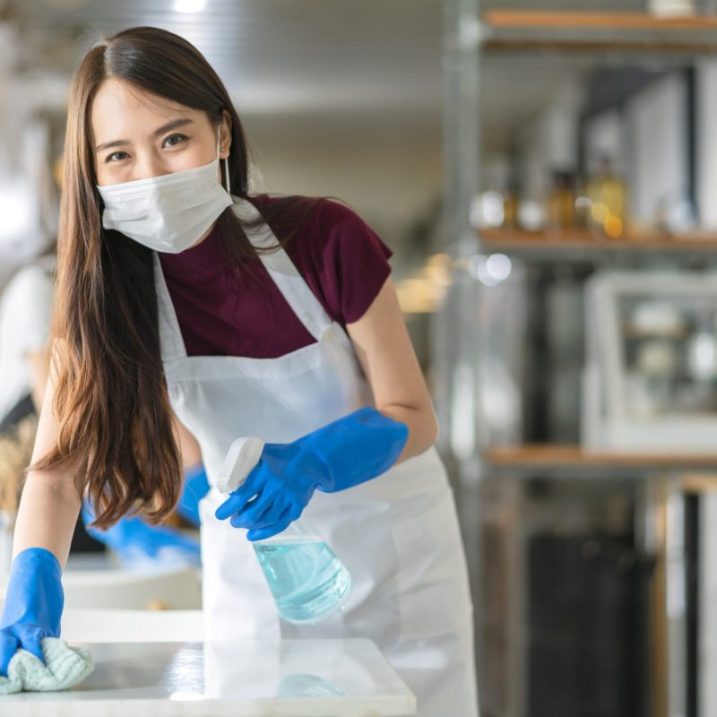 asian staff waitress wearing protection face mask apron and rubber glove cleaning table with disinfectant alcohol spray for prevent infection coronavirus in cafe coffee shop new normal concept